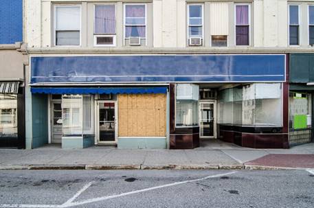 A closed storefront has boarded windows and a faded blue awning, suggesting economic hardship or transition. 